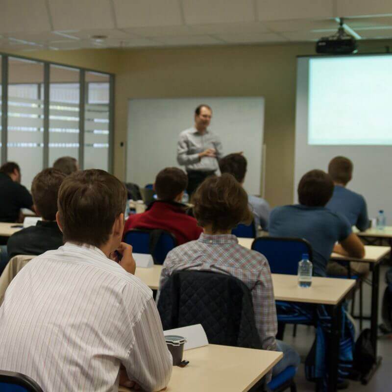 Presenter near the screen and people sitting rear and watching the conference